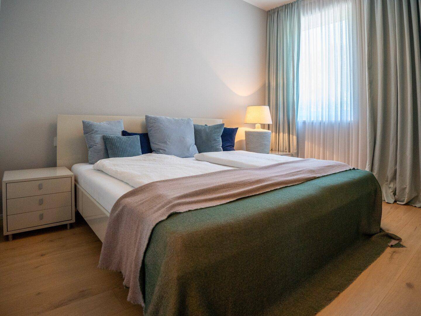 Gemütliches Schlafzimmer mit Doppelbett, Nachttischen und weichen Vorhängen, in hellen Farbtönen gehalten.