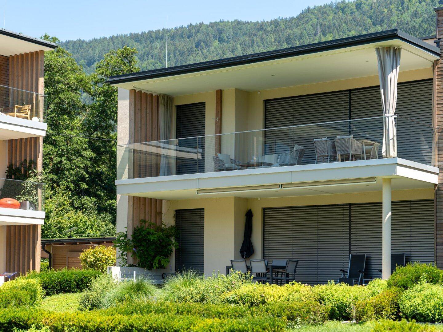 Moderne Architektur mit großzügigen Balkonen und einer Erdgeschossterrasse, umgeben von Grünflächen.