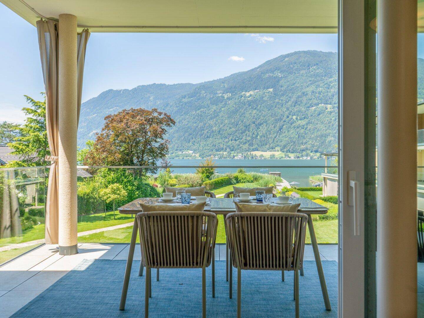 Sonniger Terrassenbereich mit Esstisch und Stühlen, bietet einen weiten Blick auf den See und die Berge.