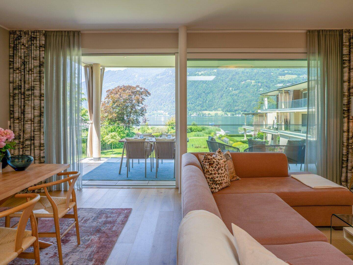 Helles Wohnzimmer mit bequemer Couch und Zugang zur Terrasse mit Panoramablick auf See und Berge.
