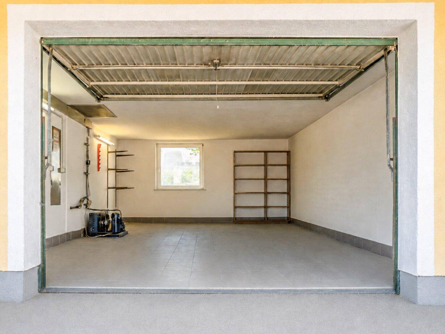 Geräumige Garage mit Betonboden, einem Fenster und Regalen für zusätzlichen Stauraum.