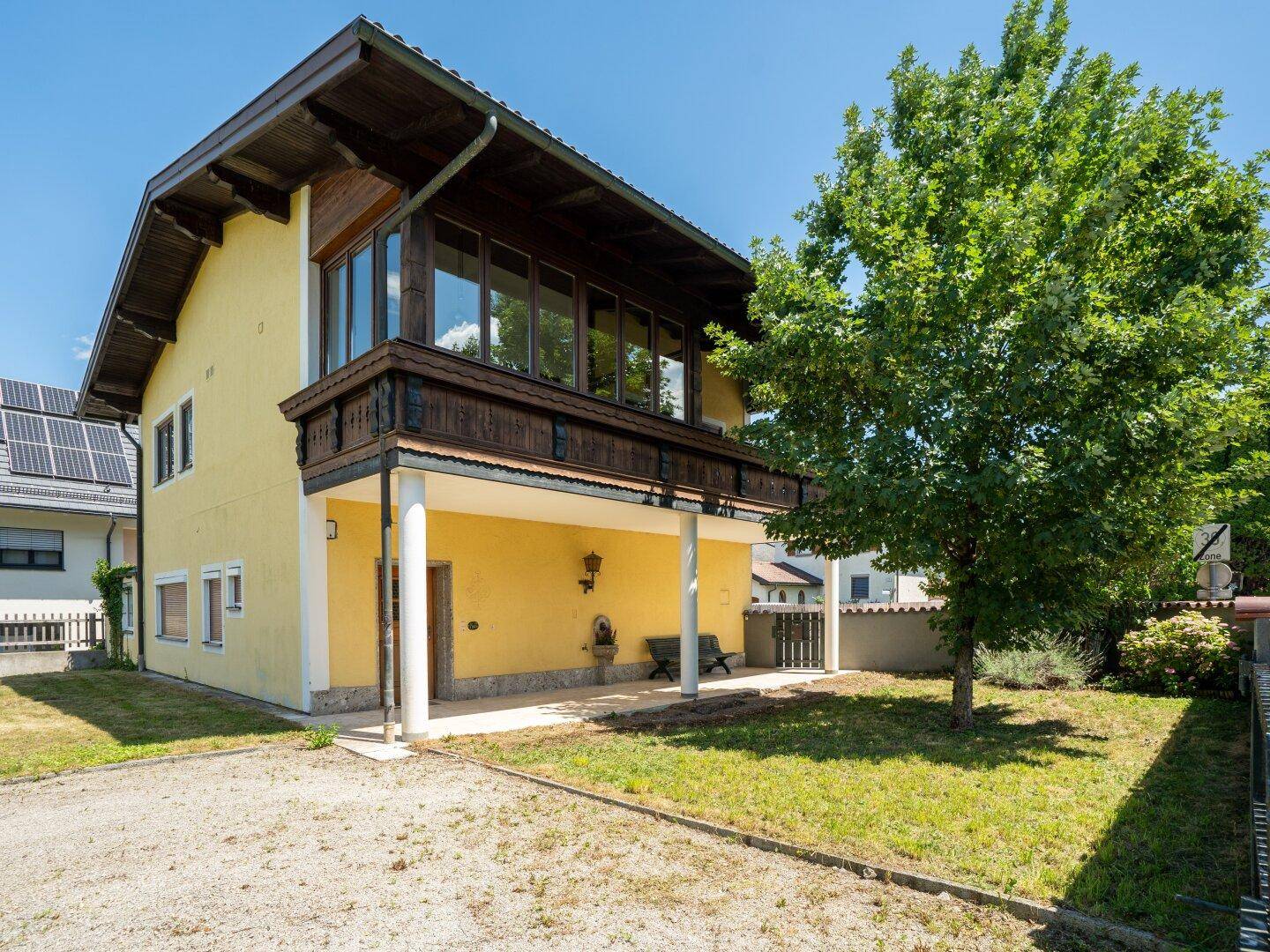 Seitenansicht des gelben Gebäudes mit Schotterauffahrt, Rasenfläche und überdachtem Balkon.