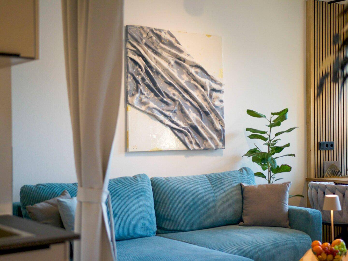 Detail des Wohnzimmers mit blauer Couch, abstrakter Kunst und grüner Zimmerpflanze.
