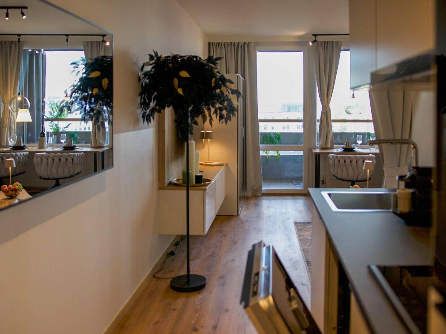 Heller Wohnbereich mit Holzboden, Essplatz am Fenster und Zugang zum Balkon.