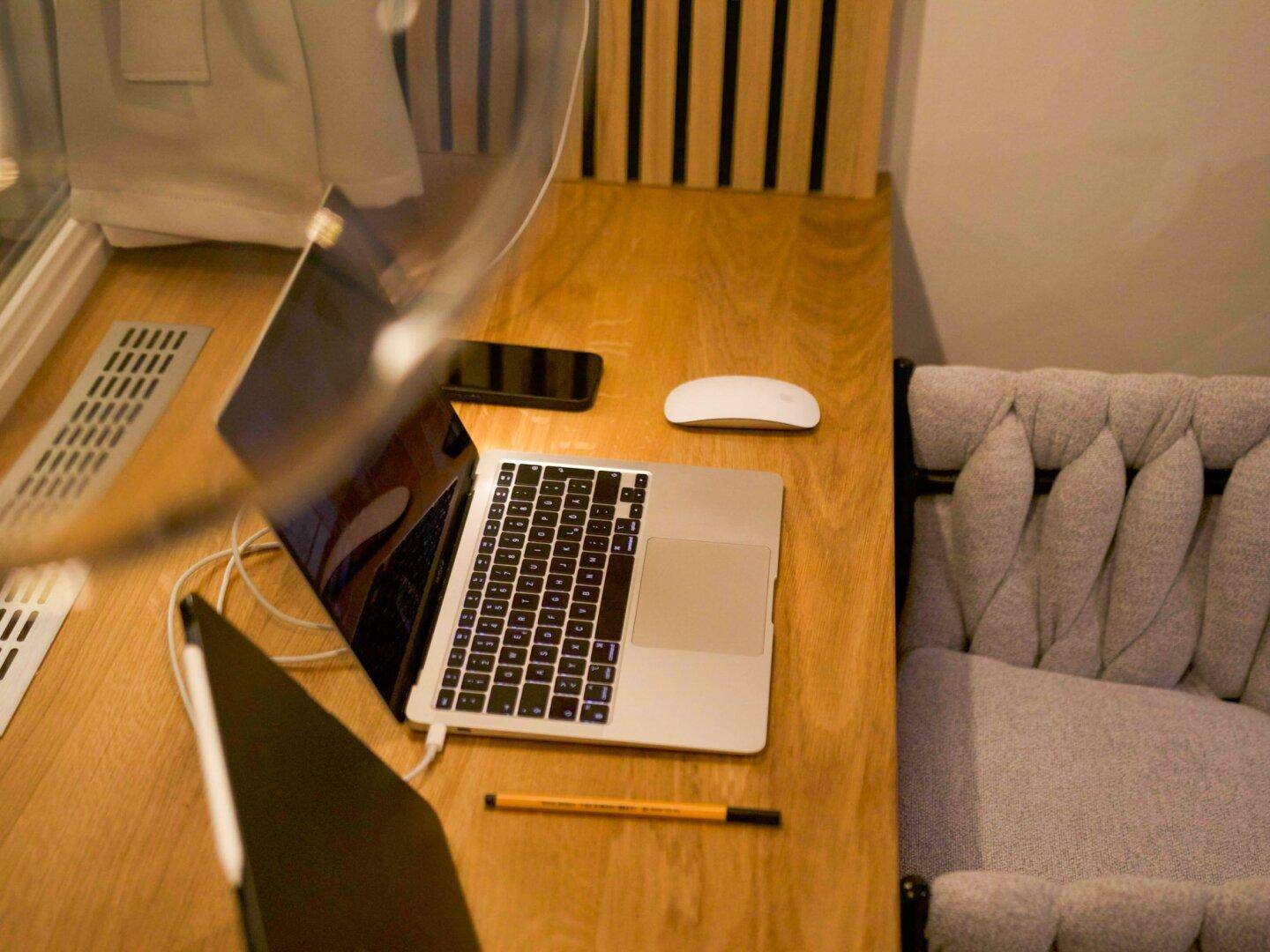 Detailansicht des Arbeitsplatzes mit Laptop, Maus und Stift auf Holztisch.