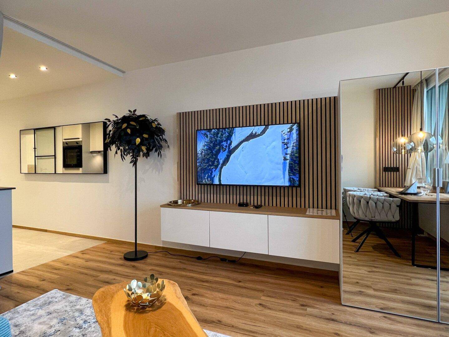 Geräumiger Wohnbereich mit Fernseher an der Wand, Holzboden und moderner Einrichtung.