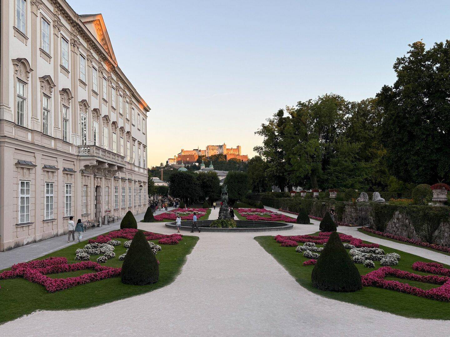 Historischer Garten mit Blumenbeeten, Springbrunnen und Blick auf die Festung Hohensalzburg.