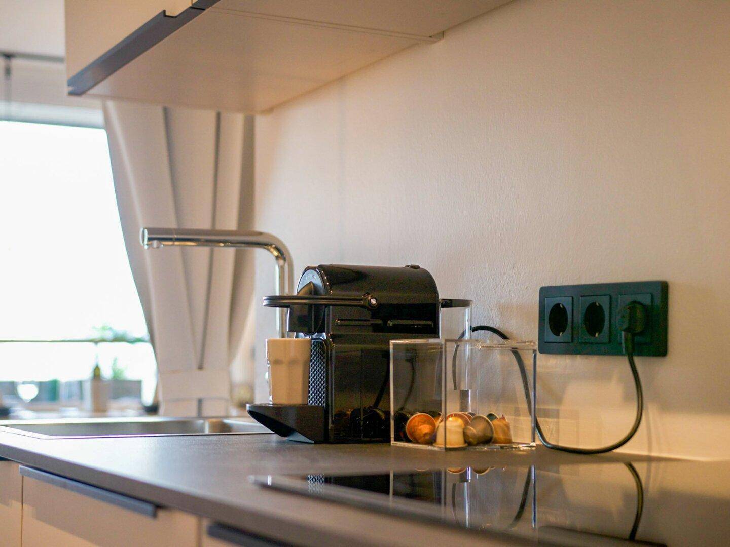 Moderne Küchenzeile mit Kaffeemaschine, Induktionskochfeld und dunkler Arbeitsplatte.