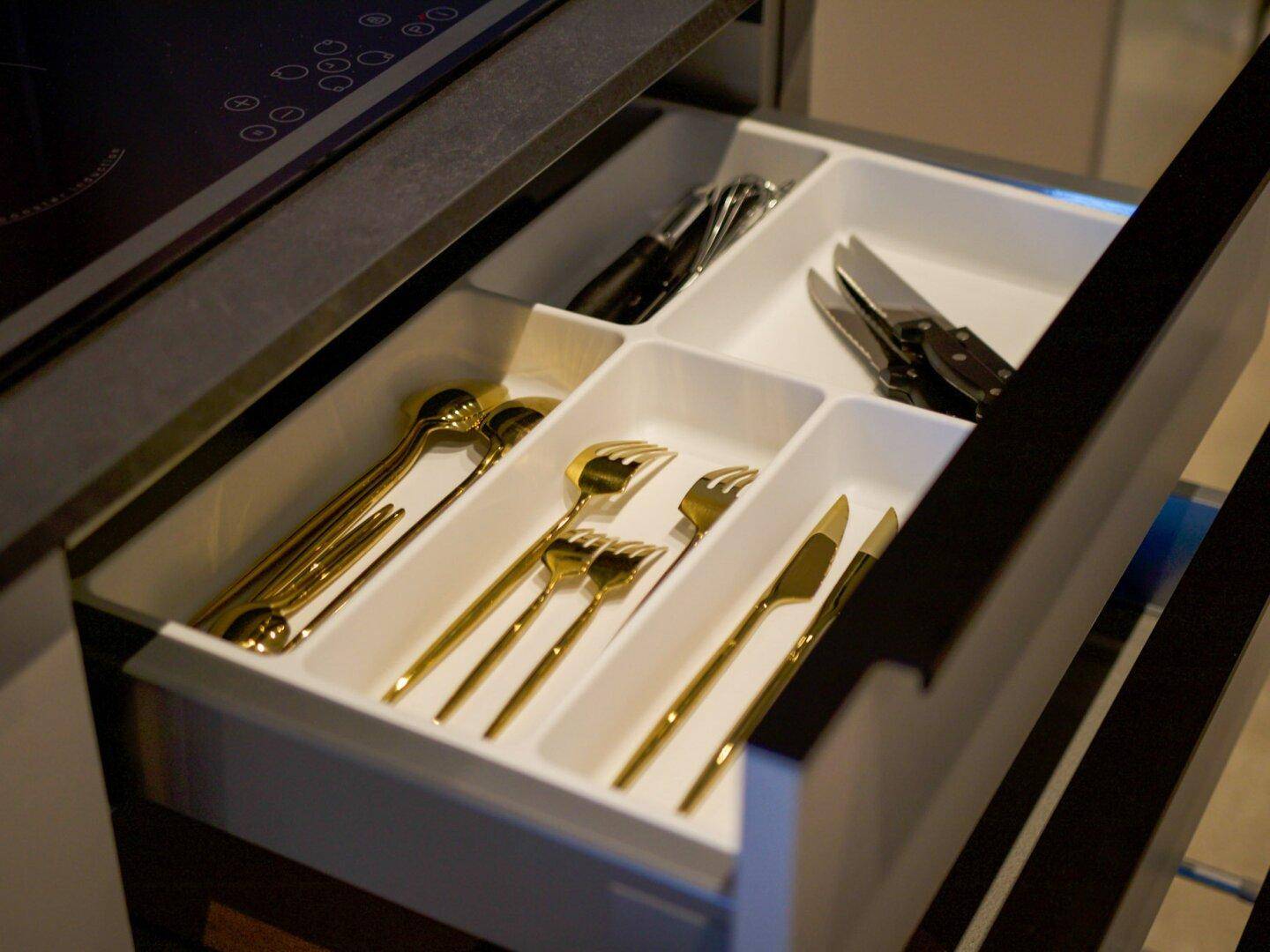 Schublade mit organisiertem Besteck, inklusive goldfarbenem Besteck, in der modernen Küche.