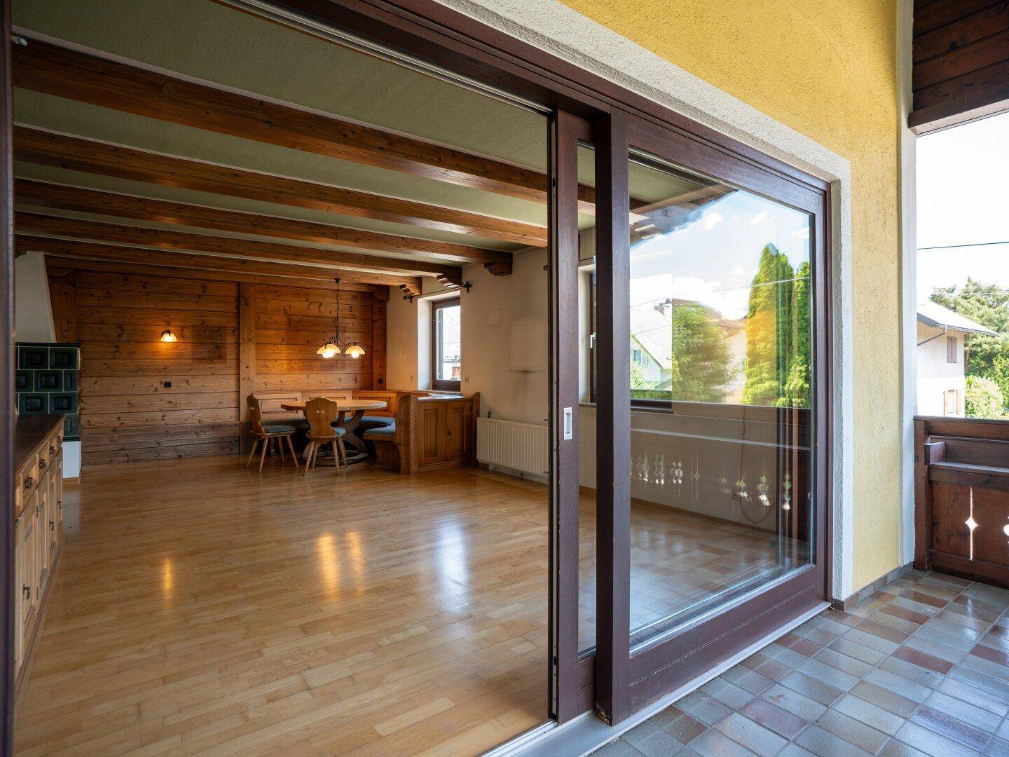 Geräumiger Wohn-Essbereich mit Holzbalkendecke, Parkettboden und Zugang zum Balkon.
