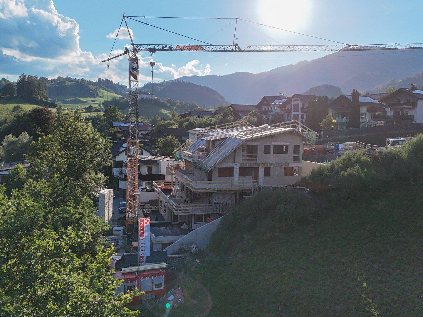 Baustelle eines modernen Hauses mit Kran und sonnigem Bergblick in einer ländlichen Umgebung.