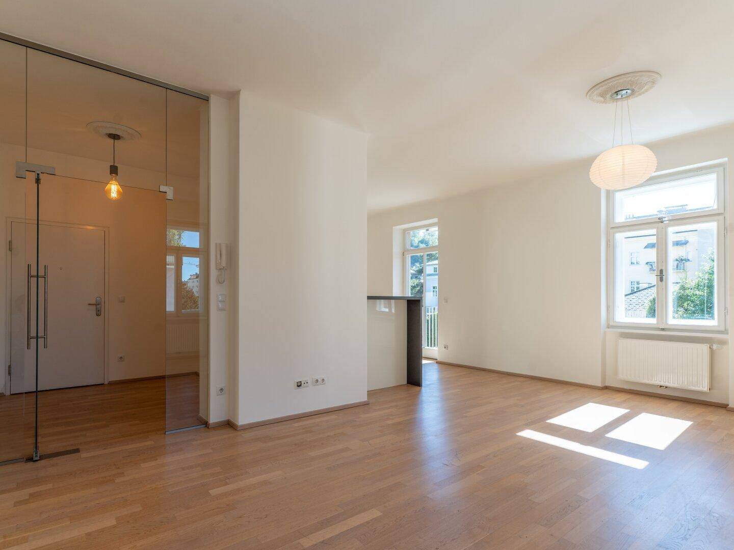 Geräumiges Wohnzimmer mit hellem Parkettboden, hohen Decken und viel Tageslicht.