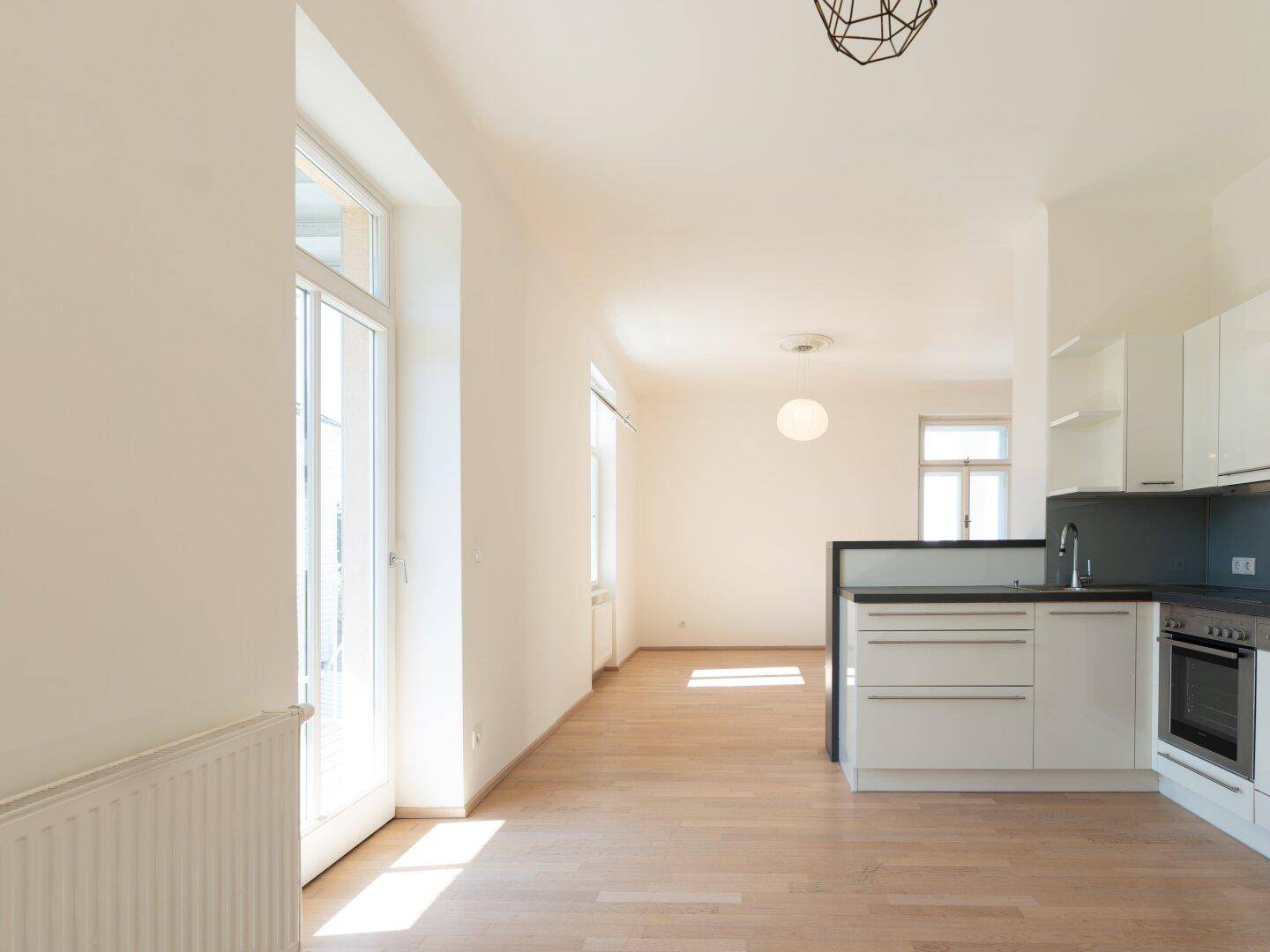 Offener Wohnbereich mit integrierter Küche und Zugang zu einem sonnigen Balkon.