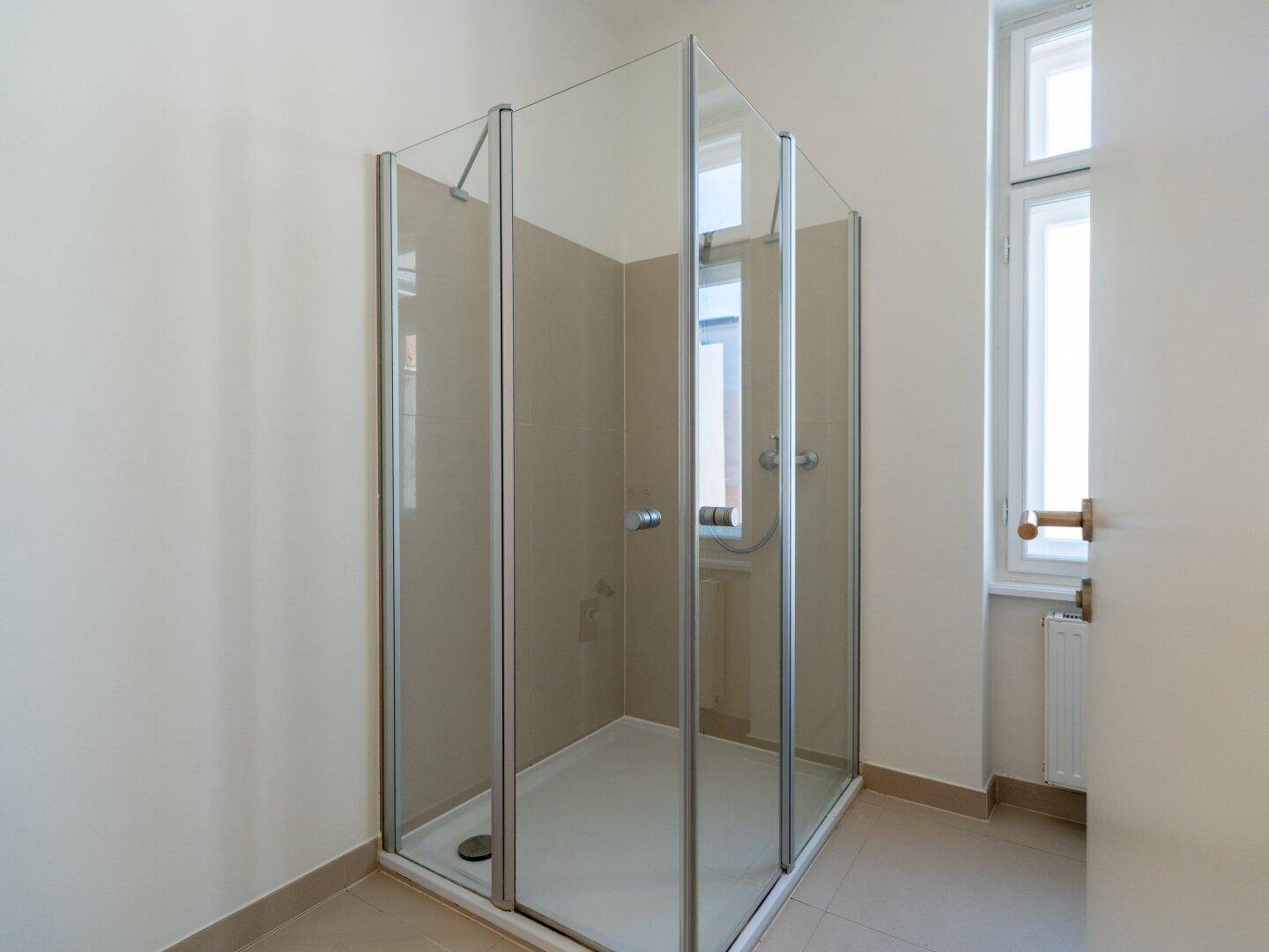 Helles Badezimmer mit geräumiger Duschkabine aus Glas und einem Fenster.