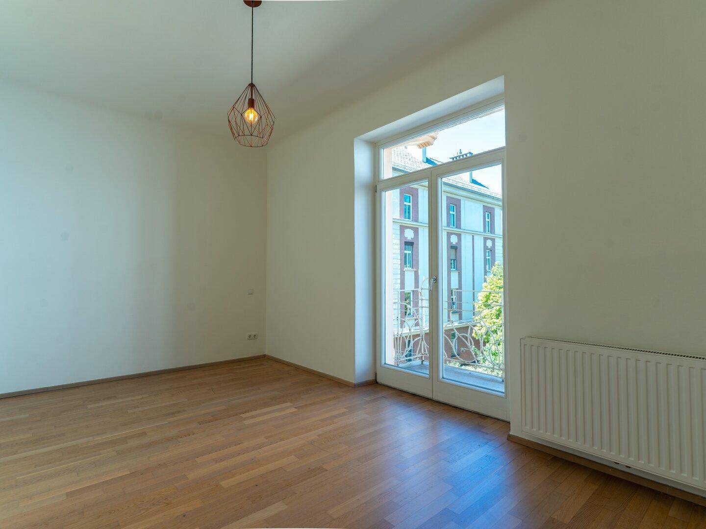 Geräumiger Raum mit Parkettboden und großem Fenster mit Zugang zum Balkon.