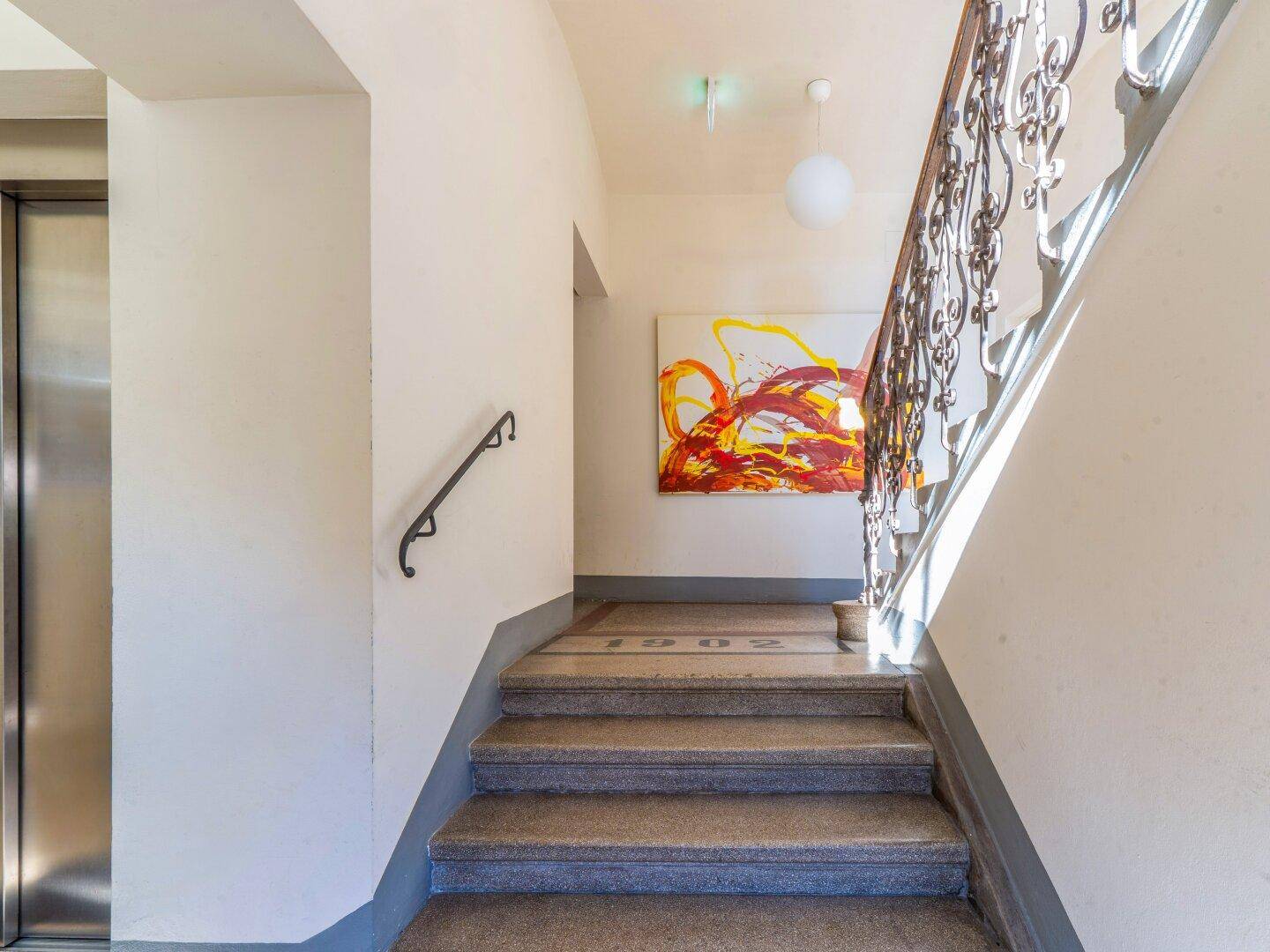 Treppenhaus mit Steinstufen, schmiedeeisernem Geländer und modernem Kunstwerk an der Wand.