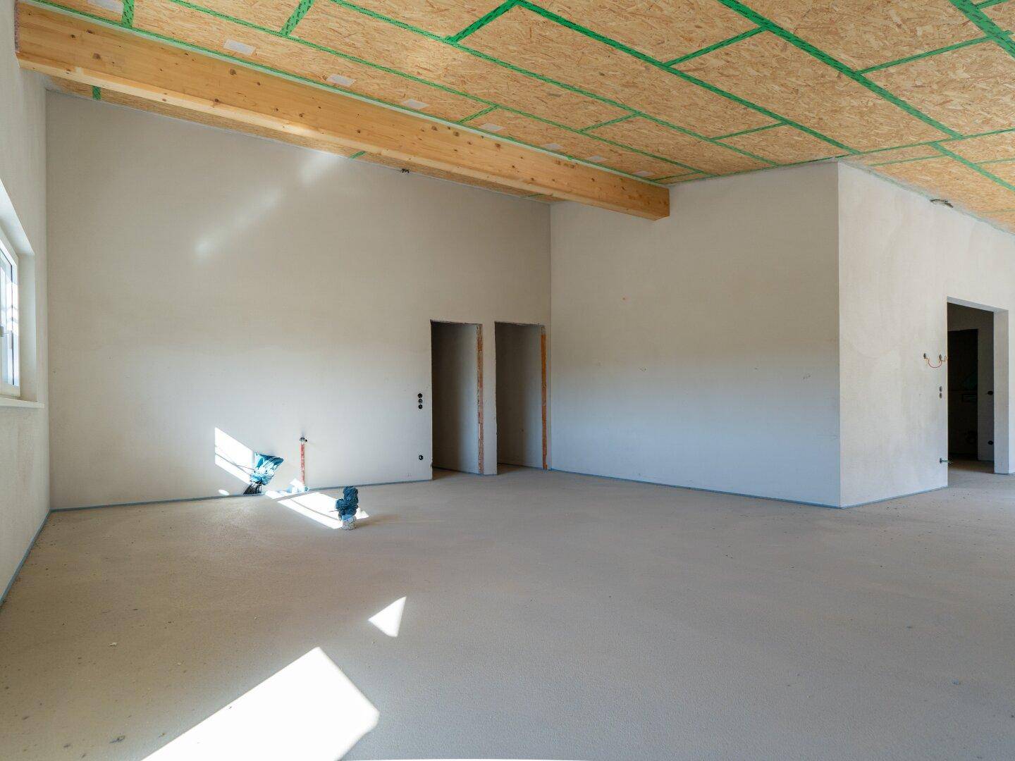 Rohbau eines Zimmers mit Holzbalken, schrägen Decken und vorbereiteten Türöffnungen.