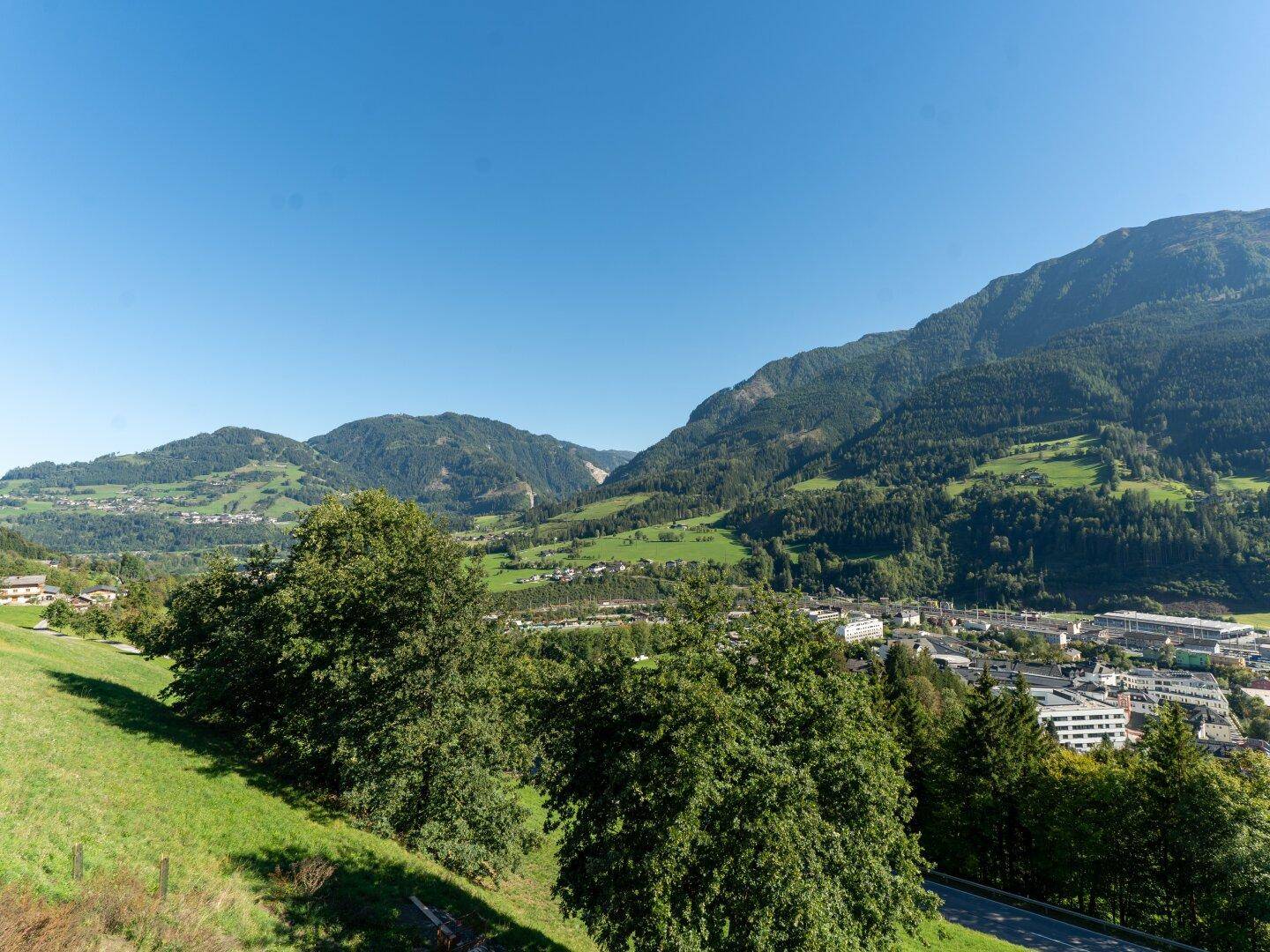 Weitläufiger Panoramablick über grüne Täler, Berge und eine Siedlung in der Ferne.