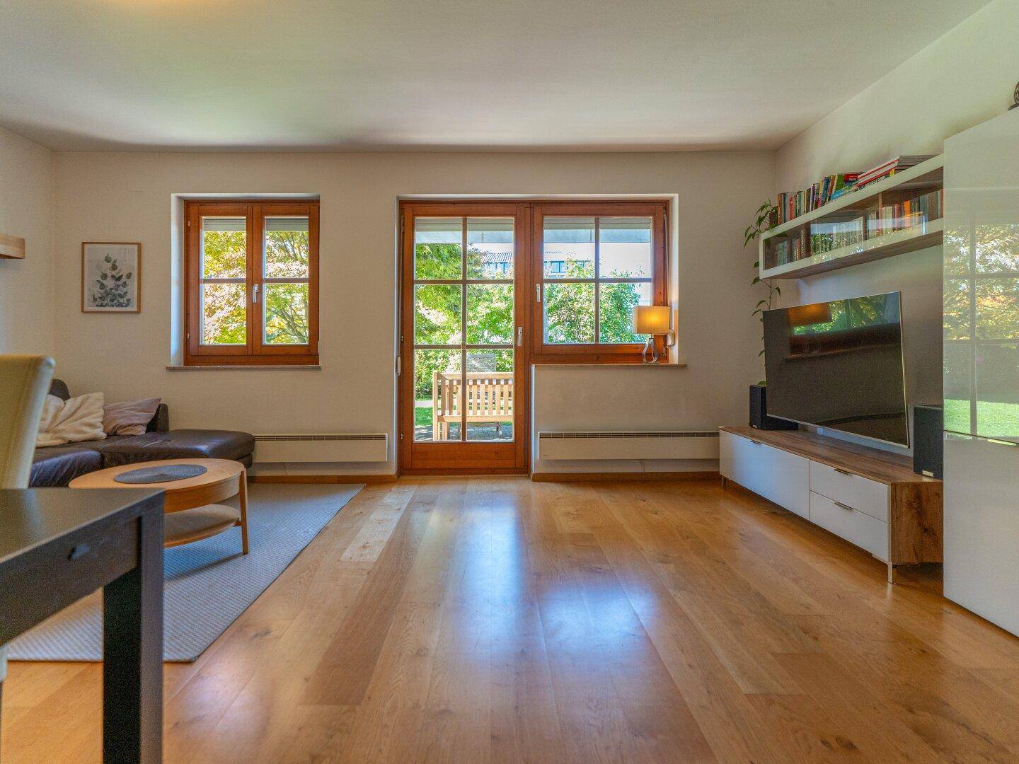 Modernes Wohnzimmer mit Holzboden, Fernseher und Bücherregal, bietet direkten Zugang zum Garten.