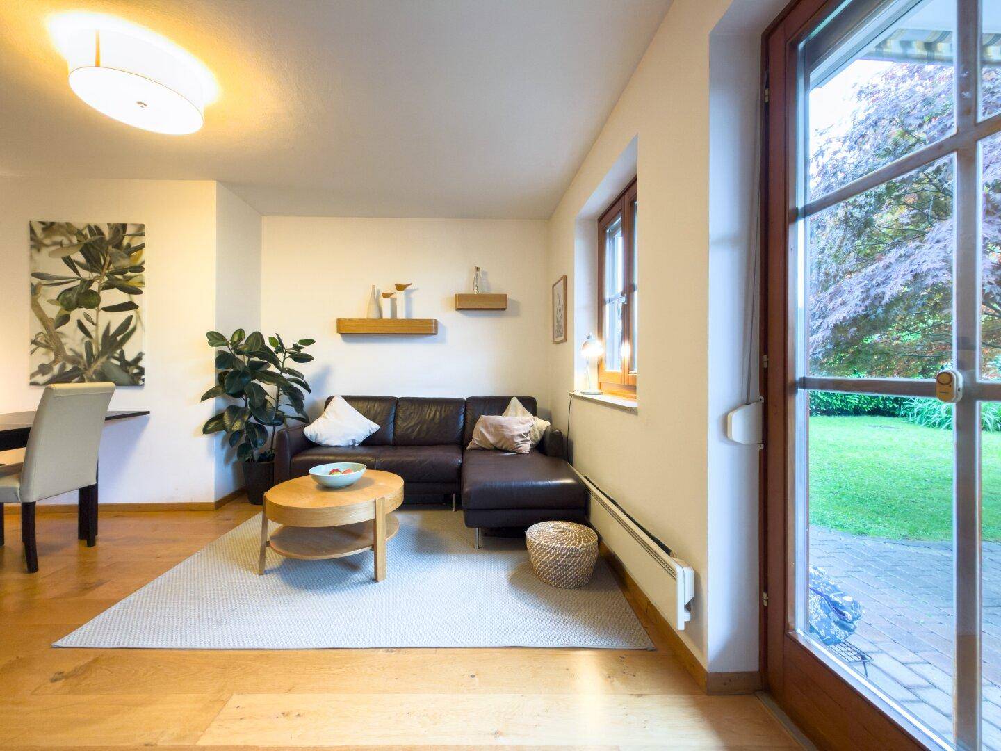 Gemütliches Wohnzimmer mit Holzboden, Ledersofa und großzügigem Zugang zur Terrasse und zum Garten.