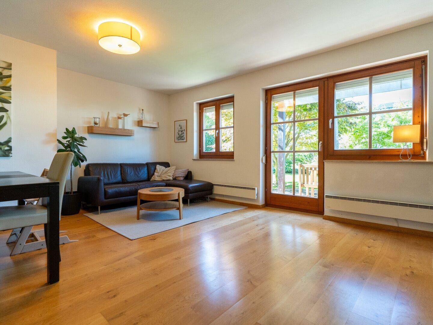 Helles Wohnzimmer mit Holzboden, bequemer Ledercouch und direktem Zugang zum grünen Garten.