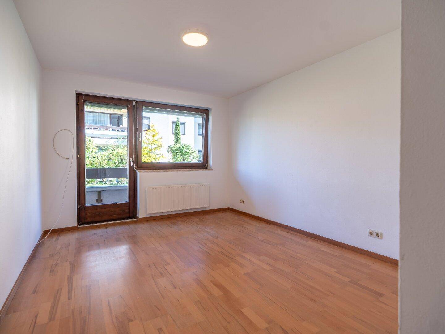 Helles Zimmer mit Holzboden und Zugang zu einem Balkon, ideal als Schlaf- oder Gästezimmer.