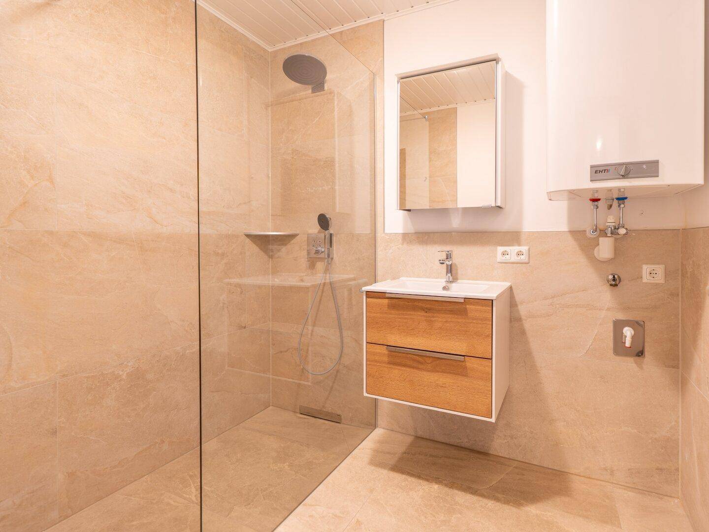 Modernes Badezimmer mit beigefarbenen Fliesen, ebenerdiger Dusche und Waschbecken mit Unterschrank.