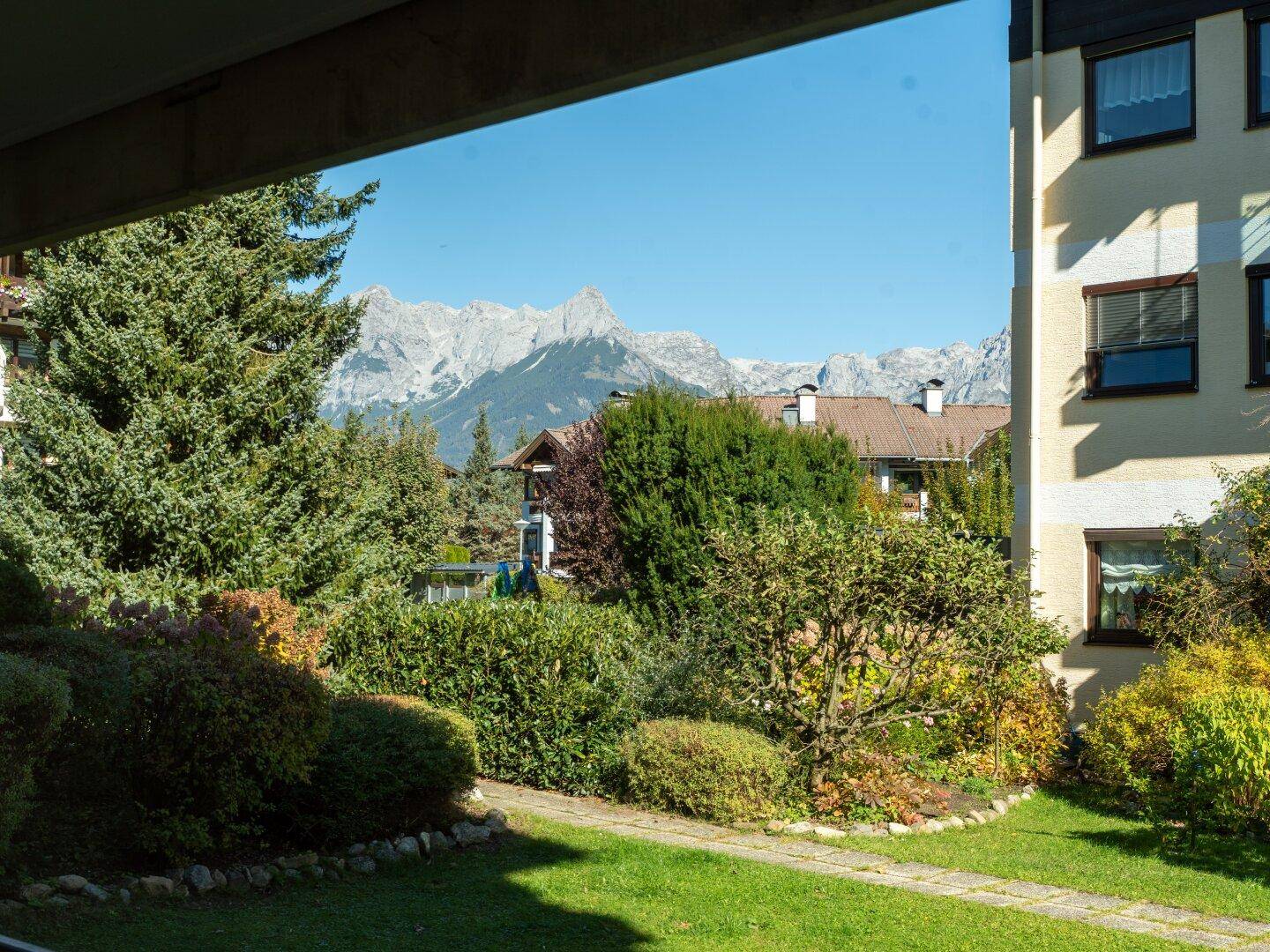 Grüner Gartenbereich mit gepflegten Hecken und Bäumen, im Hintergrund die Berge.
