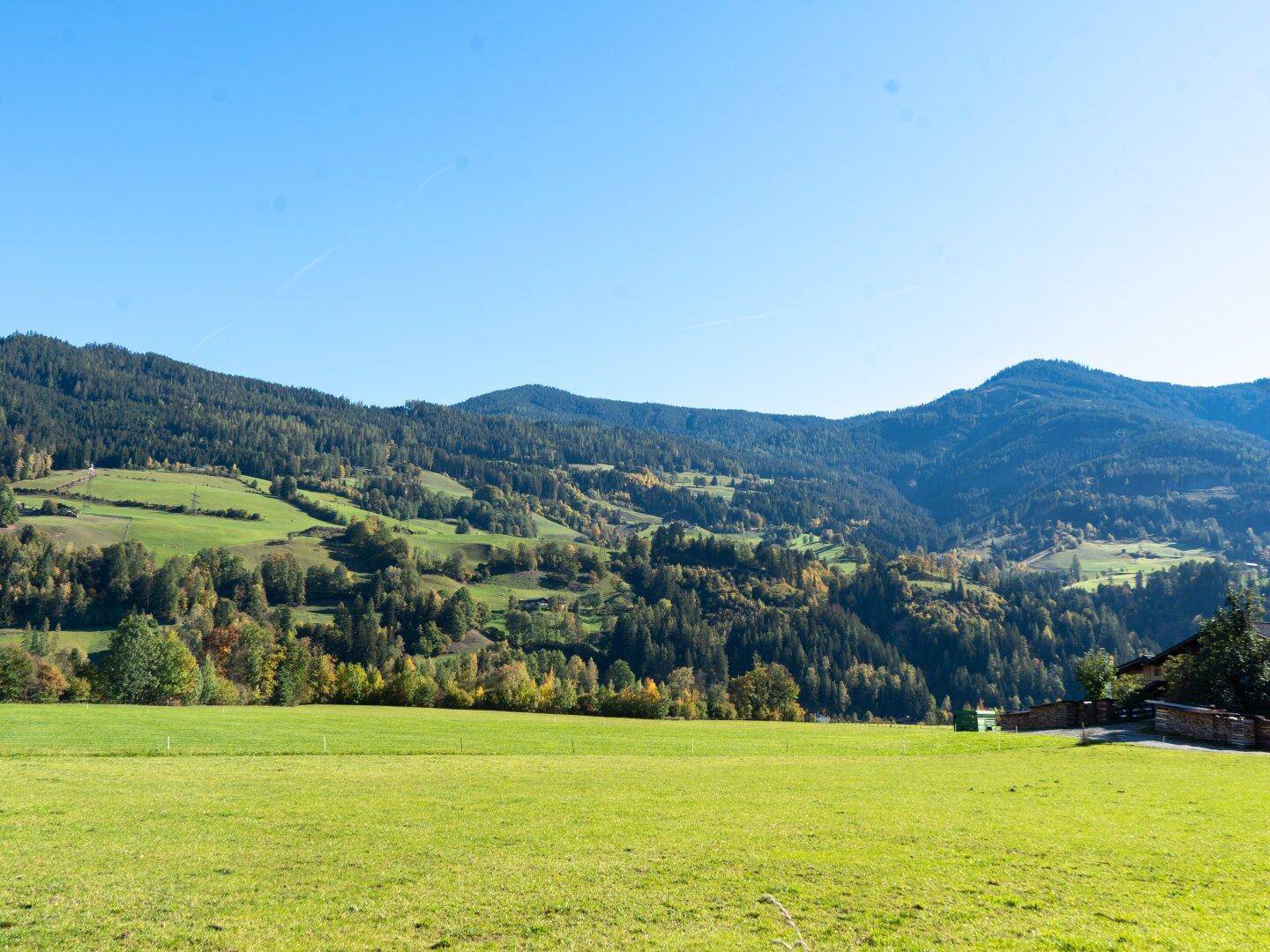 Weitläufige Landschaft mit grünen Hügeln und bewaldeten Bergen unter klarem Himmel.