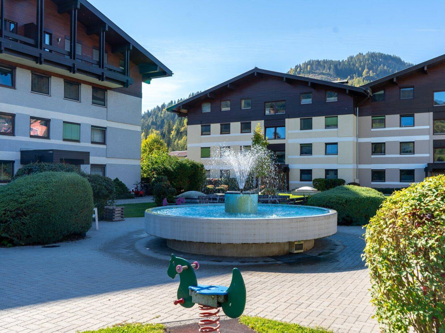 Attraktiver Innenhof mit Springbrunnen und Kinderspielgerät, umgeben von Wohngebäuden.