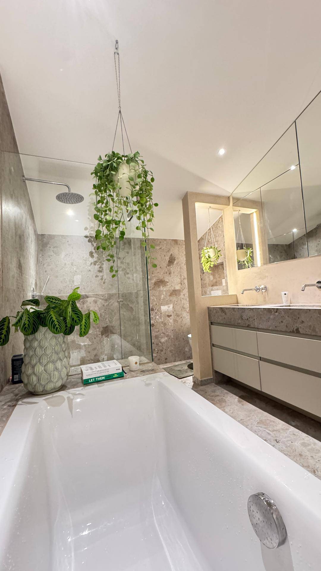 Modernes Badezimmer mit Badewanne, Regendusche und hängenden Pflanzen.