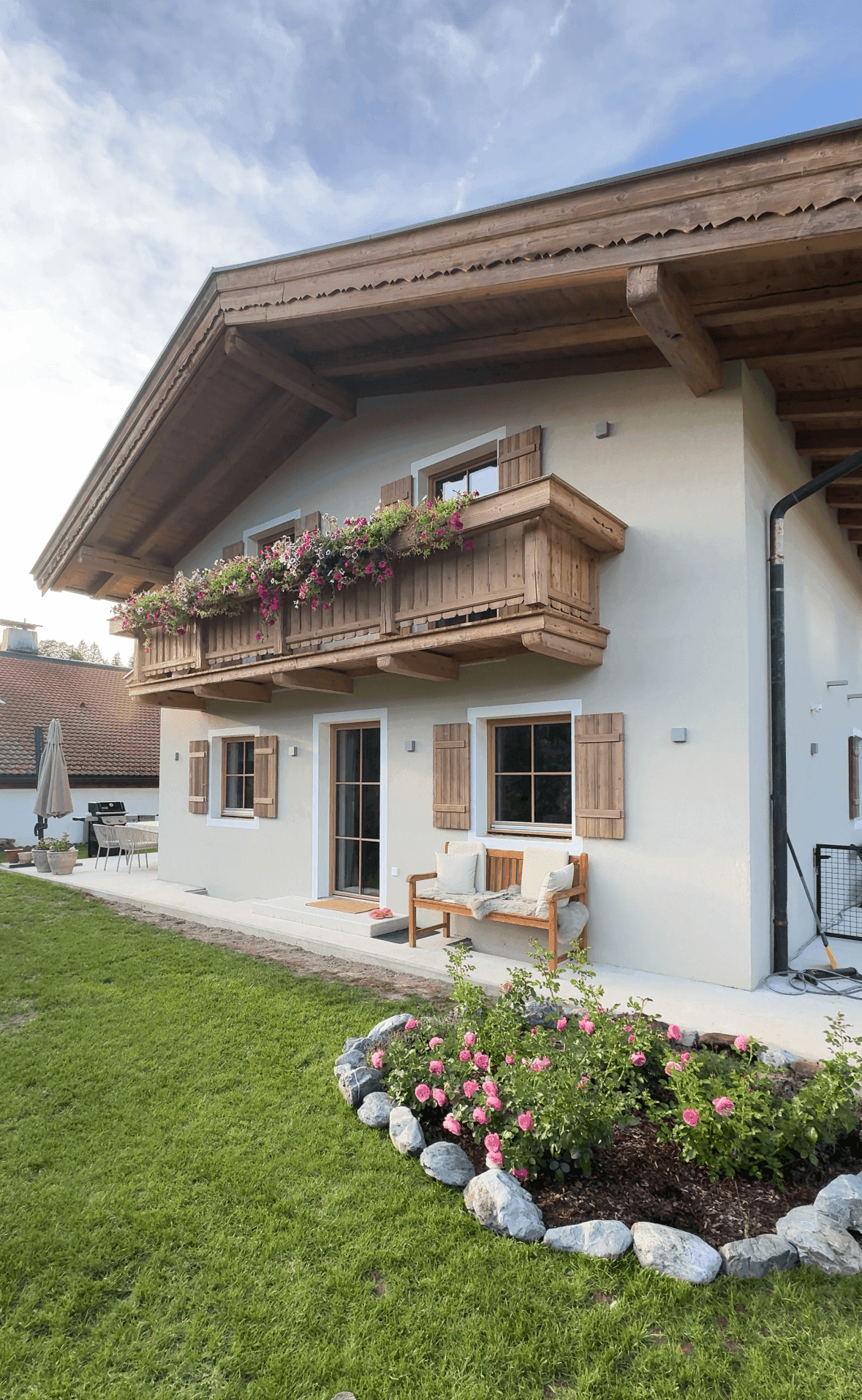 Seitenansicht des Hauses mit gepflegtem Garten, blühenden Rosen und einer Holzbank.