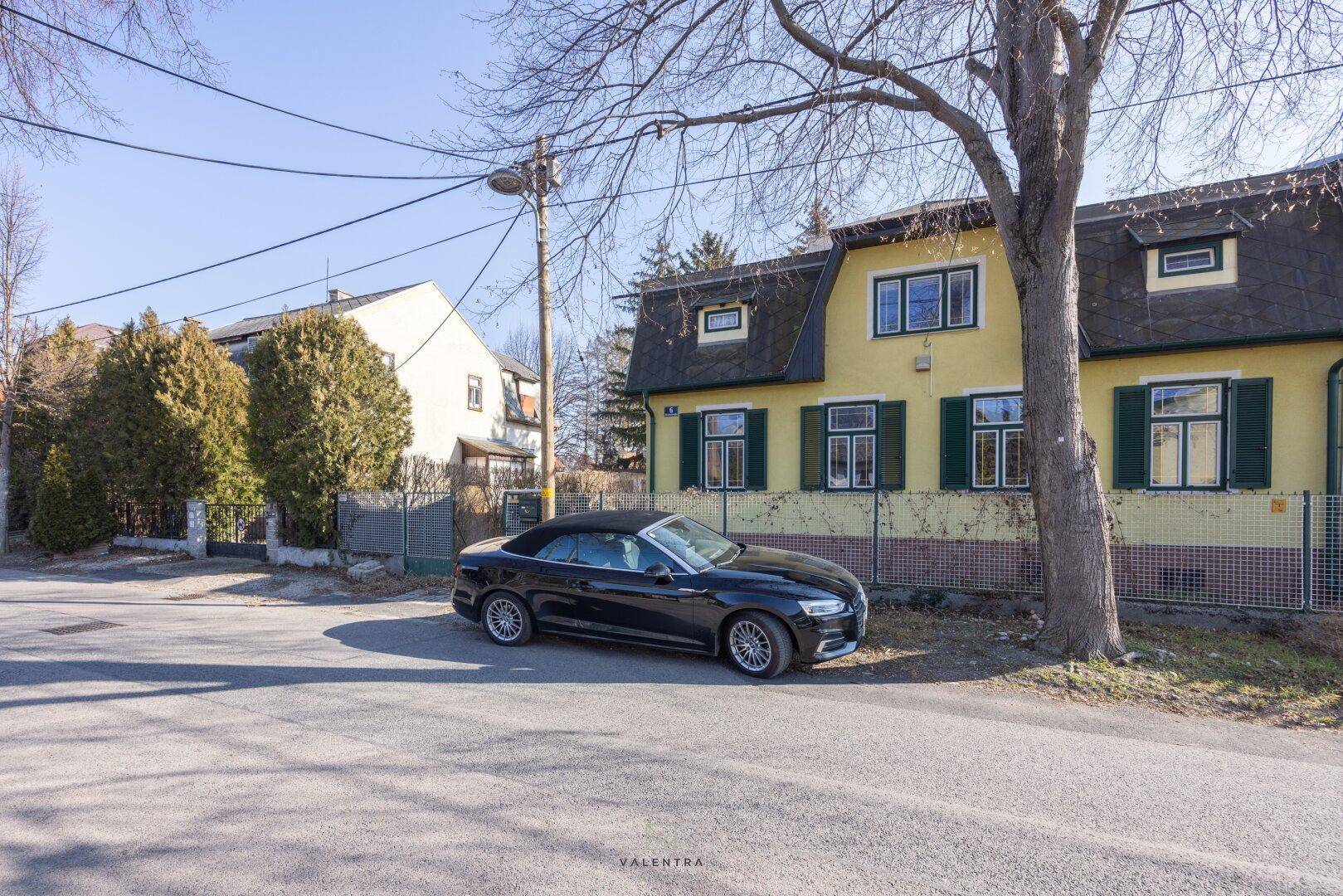 Straßenansicht des gelben Hauses mit Mansarddach, grünen Fensterläden und geparktem Auto.