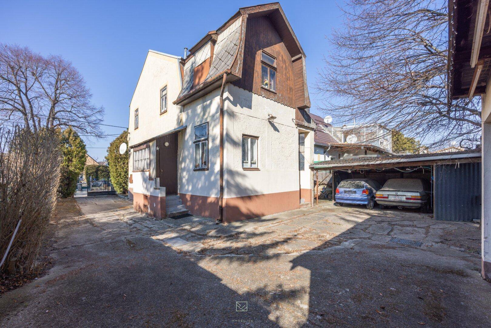 Historisches Wohnhaus mit Mansarddach und einem Carport für Fahrzeuge auf dem Grundstück.