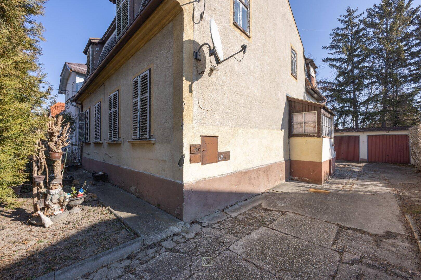 Seitenansicht des Hauses mit Fensterläden, einem kleinen Anbau und einer Zufahrt zur Garage.