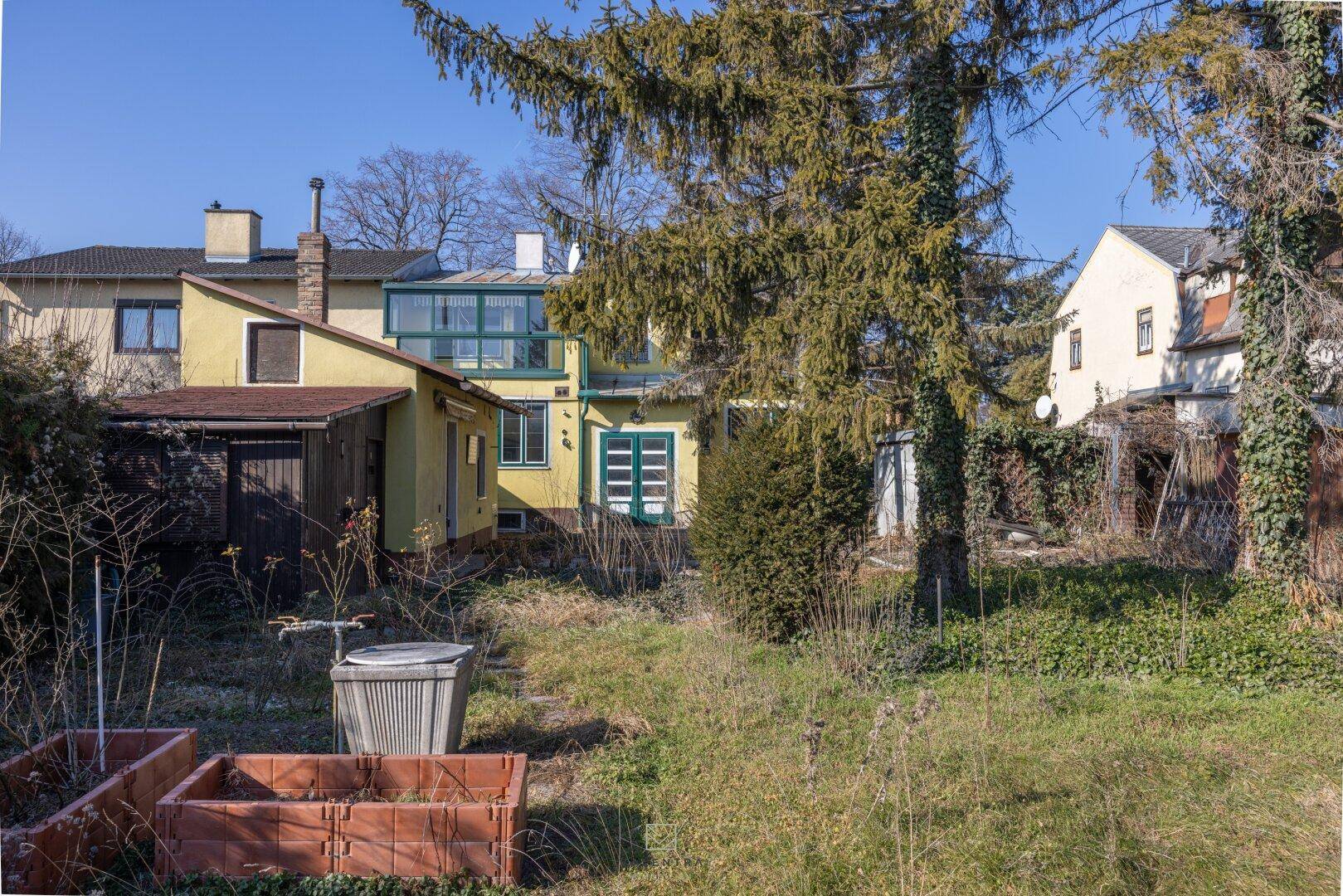 Hinteransicht des Hauses mit einem Anbau, Gartenbereich und Hochbeeten für den Anbau von Pflanzen.