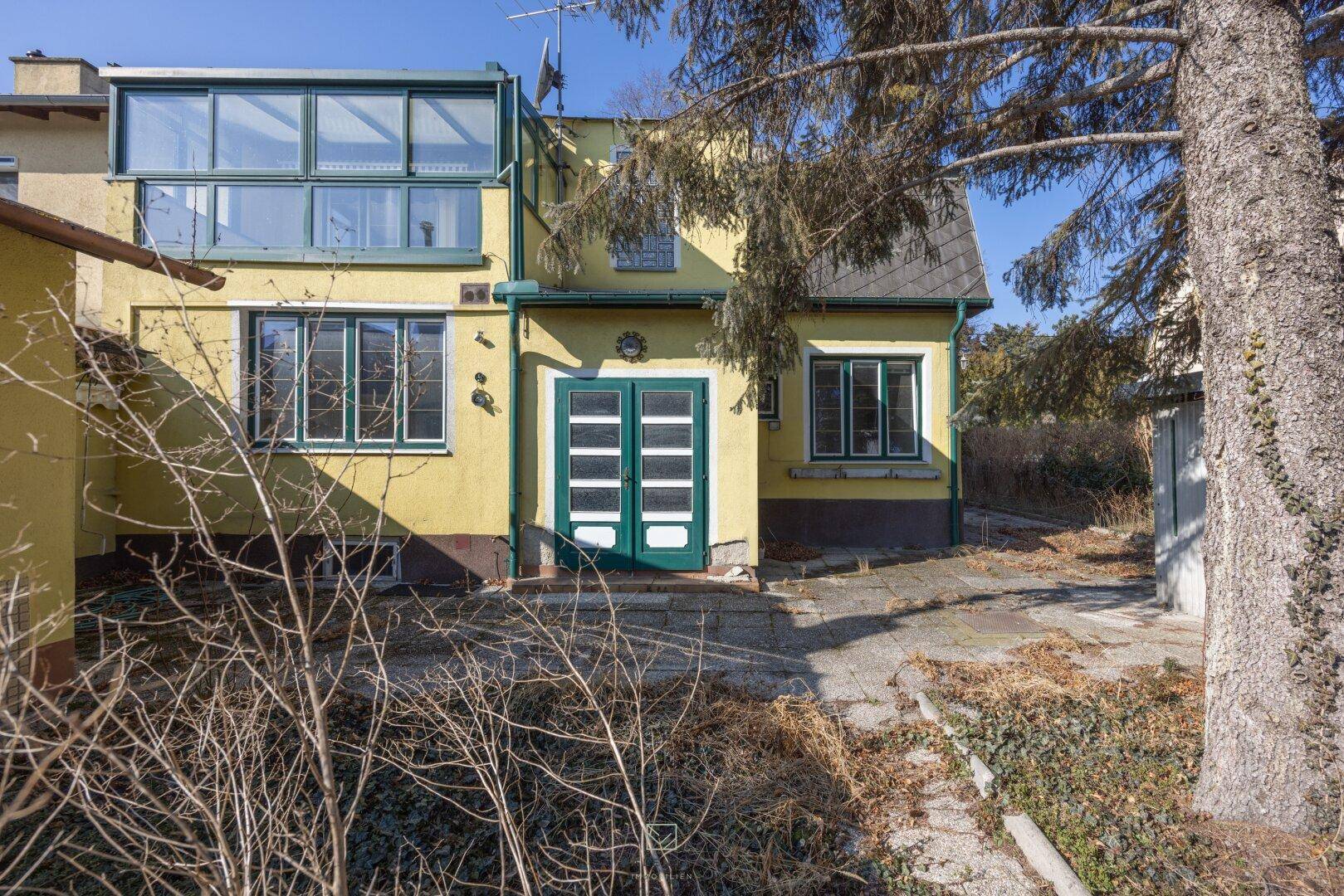 Rückseite des Hauses mit einem verglasten Wintergarten und grünen Türen.