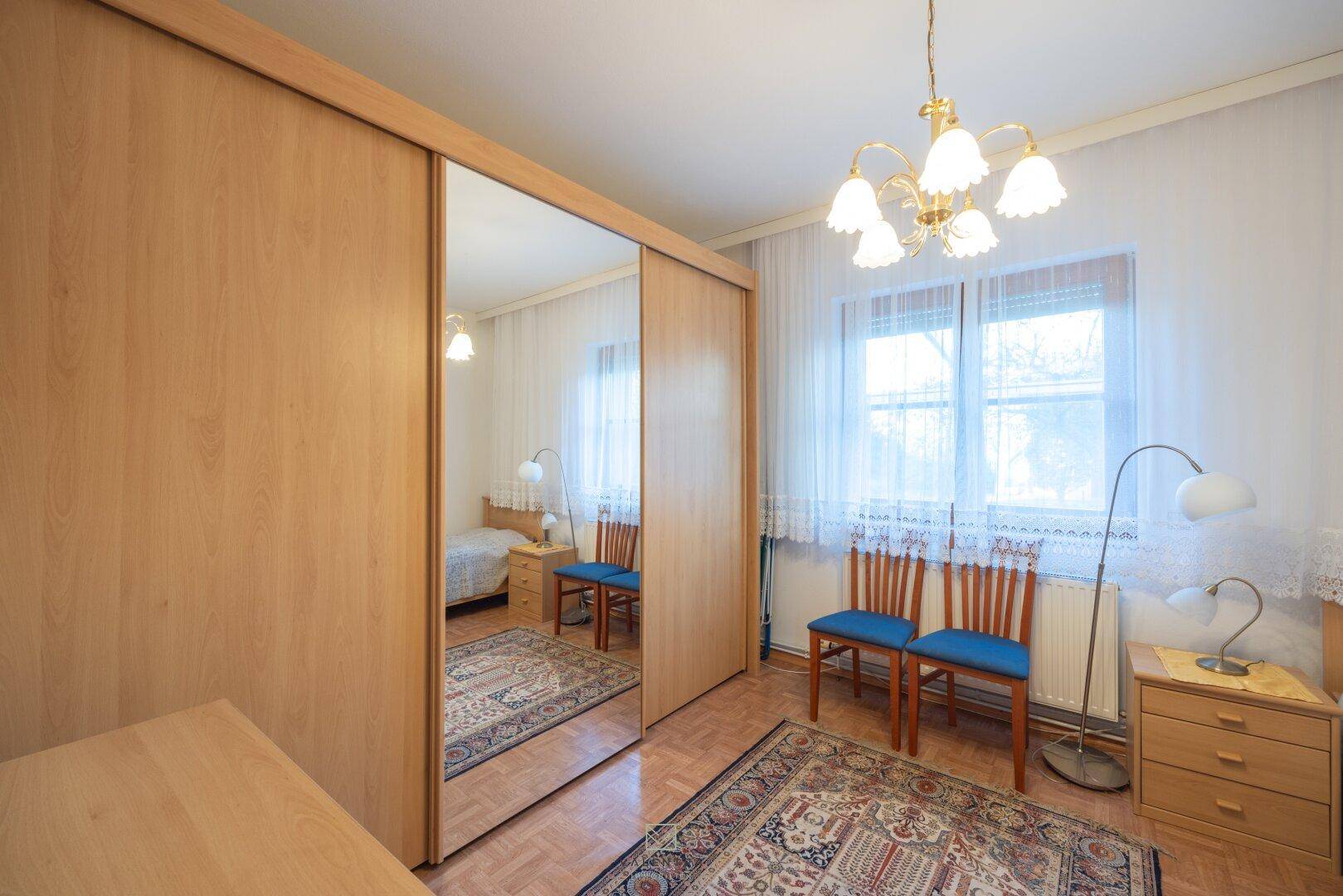 Schlafzimmer mit großem Spiegelschrank, Einzelbett und Fenster mit viel Tageslicht.
