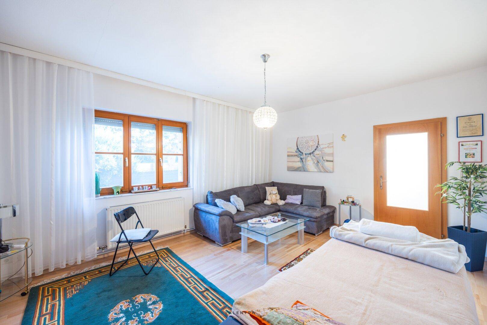Helles Wohnzimmer mit Sofa, Couchtisch und Blick auf den Garten durch das Fenster.