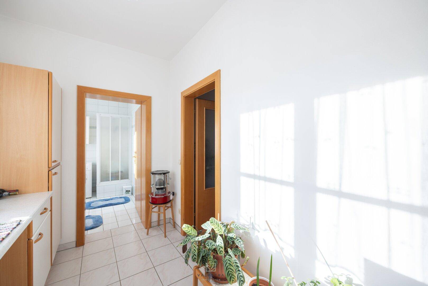 Helle Küche mit Fliesenboden und Zugang zu einem Badezimmer, durchflutet von Sonnenlicht.