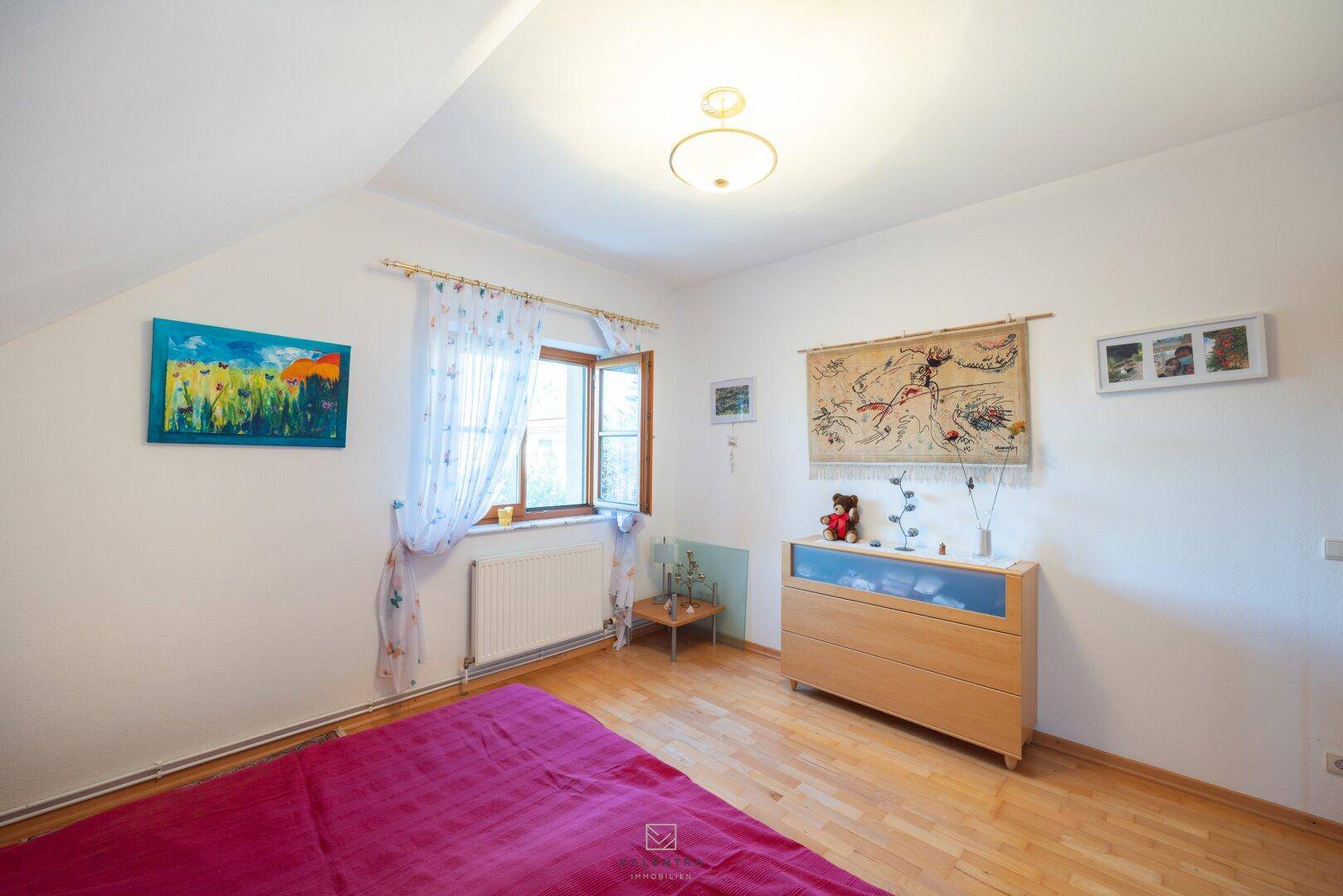 Helles Schlafzimmer mit Holzboden, Dachschräge und einem Fenster für natürliches Licht.