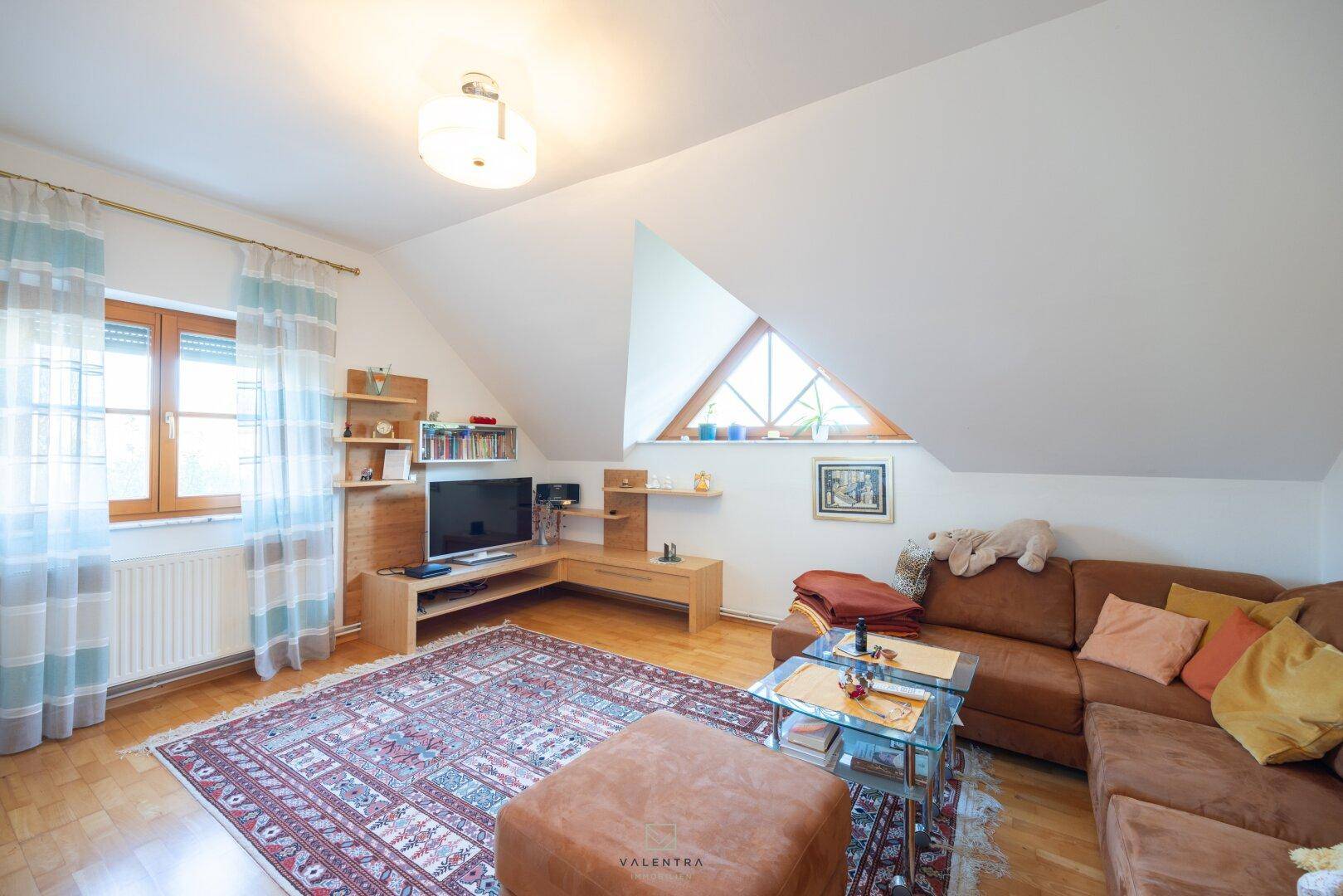 Gemütliches Wohnzimmer im Dachgeschoss mit Schrägen, Holzboden und großem Teppich.