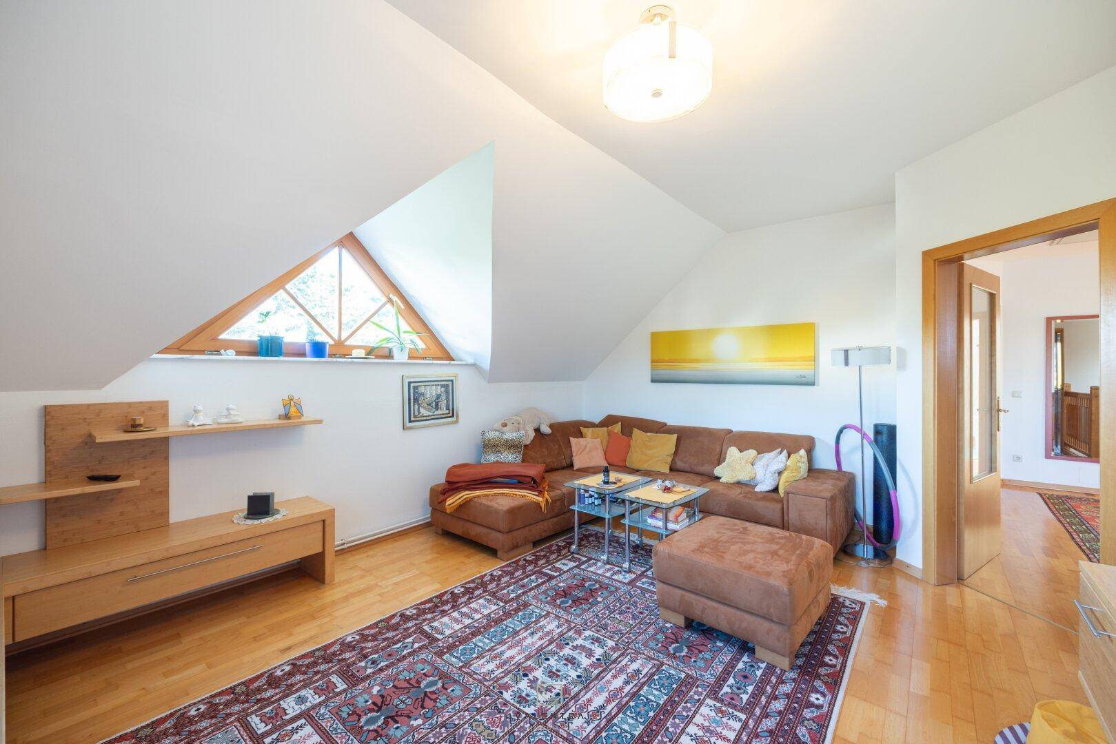 Helles Wohnzimmer im Dachgeschoss mit bequemer Couch, Holzboden und Dachfenster.