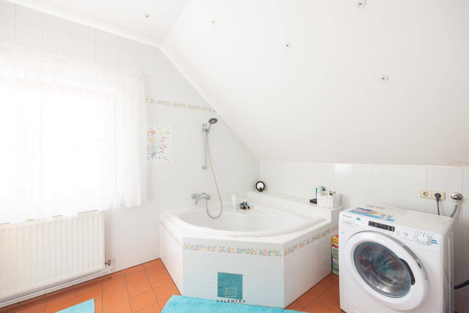 Geräumiges Badezimmer mit Eckbadewanne, Waschmaschine und Fenster unter der Dachschräge.