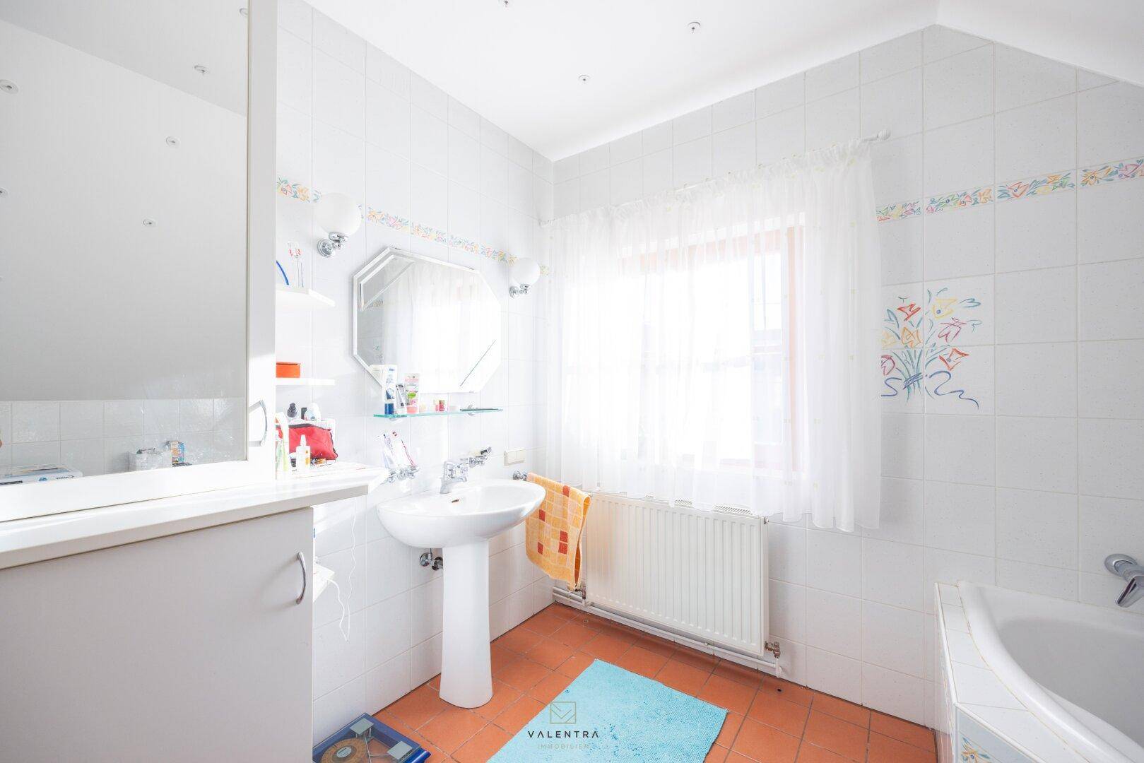 Helles Badezimmer mit Waschbecken, Spiegel und Fenster, gefliestem Boden und Dachschräge.