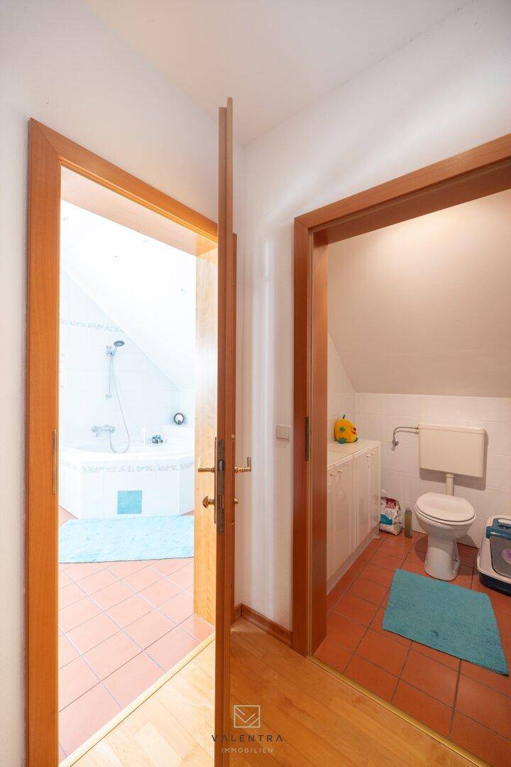Flur mit Holzboden und Zugang zu Badezimmer und separatem WC, beide mit Dachschräge.