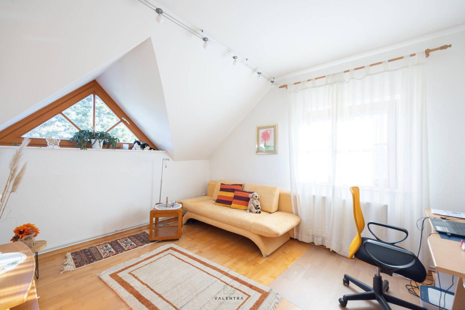 Helles Arbeitszimmer mit Sofa, Schreibtisch und besonderem Dreiecksfenster unter der Dachschräge.