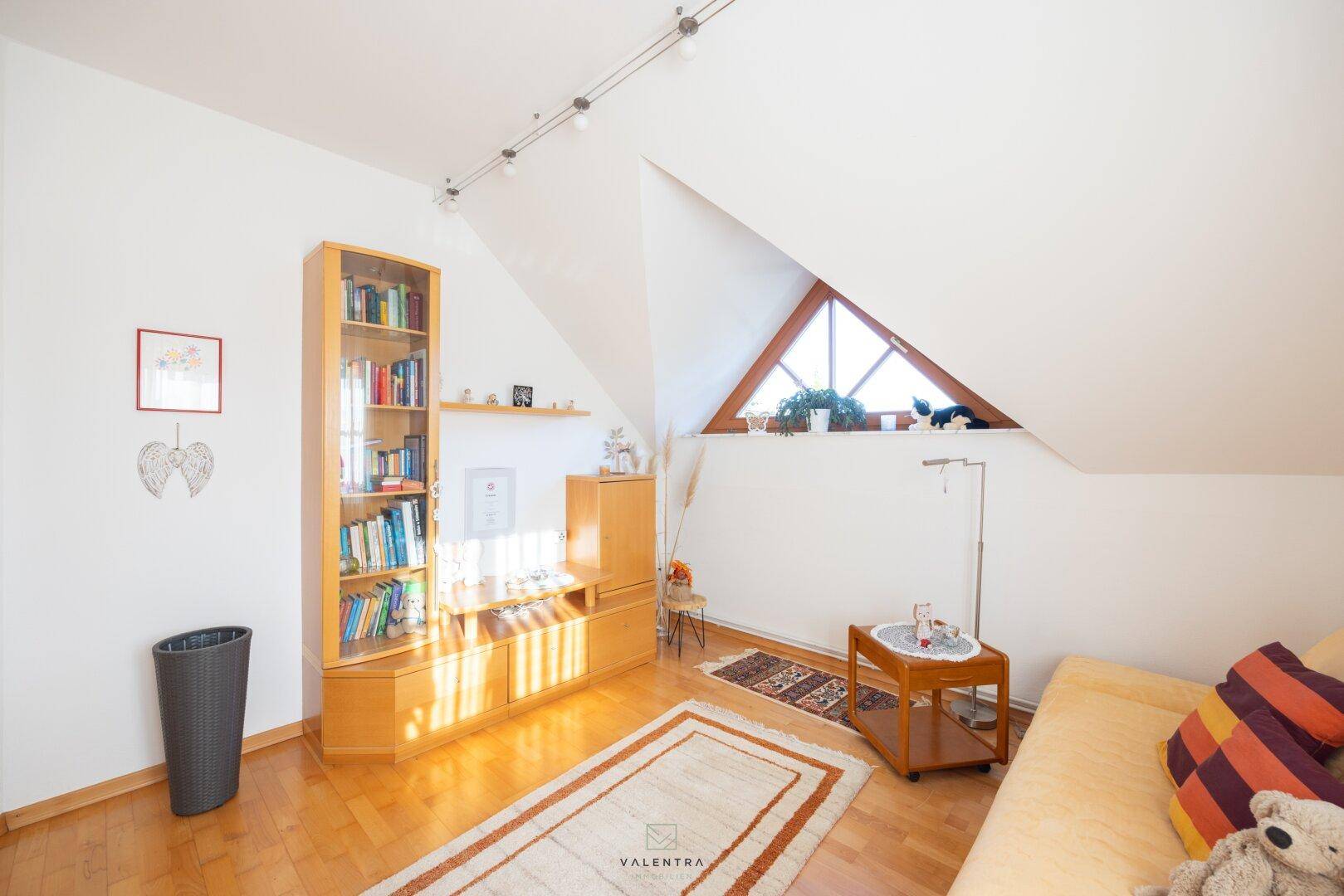 Gemütliches Zimmer mit Bücherregal, Sofa und viel Tageslicht durch das Dreiecksfenster.