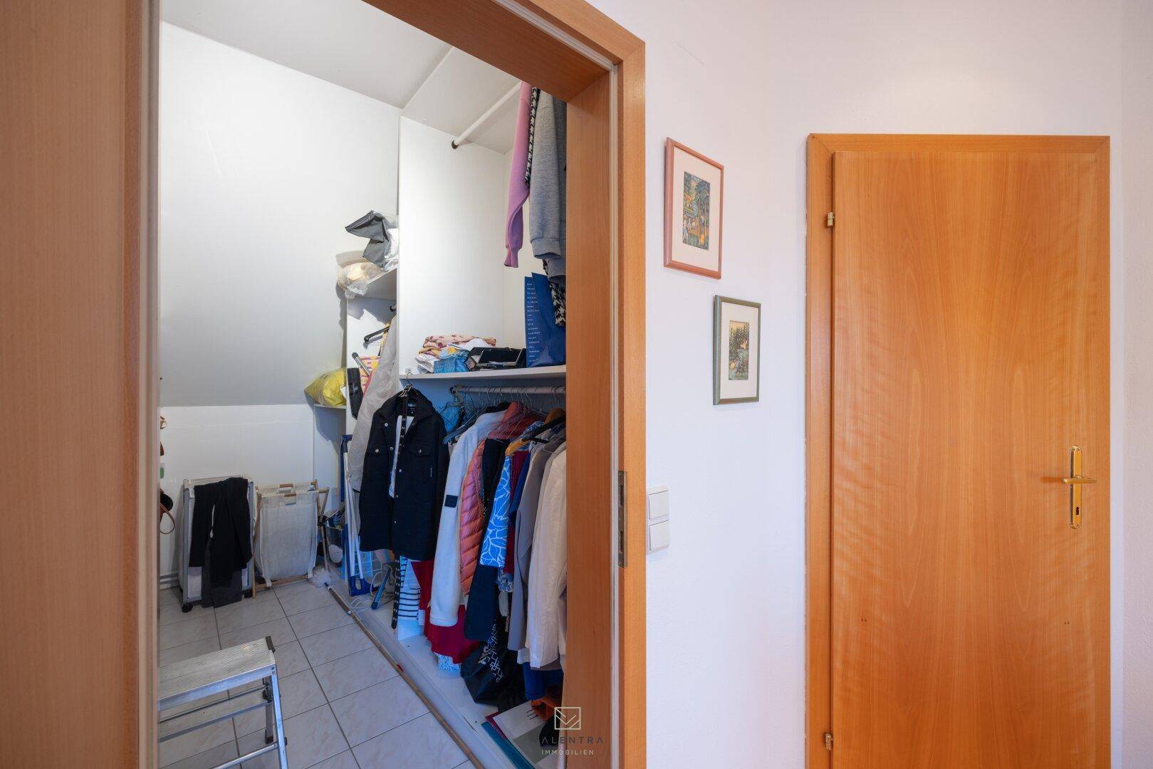 Begehbarer Kleiderschrank mit viel Stauraum, Regalen und Dachschräge, gefliestem Boden.