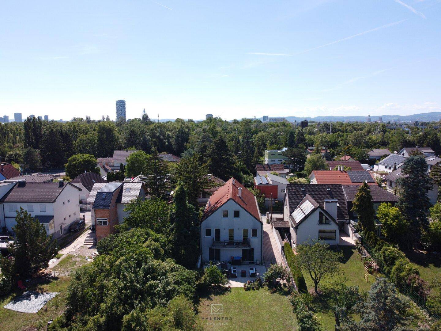 Luftaufnahme eines Wohnhauses mit großem Garten in einer grünen Vorstadtgegend mit Stadtblick.